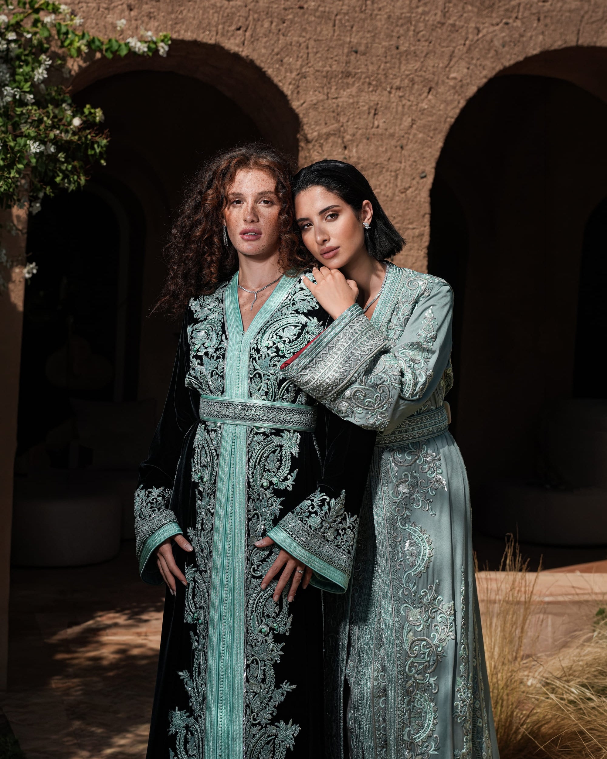 Cypress Portico deep green velvet Moroccan kaftan with sea-green embroidery, shown alongside a second look