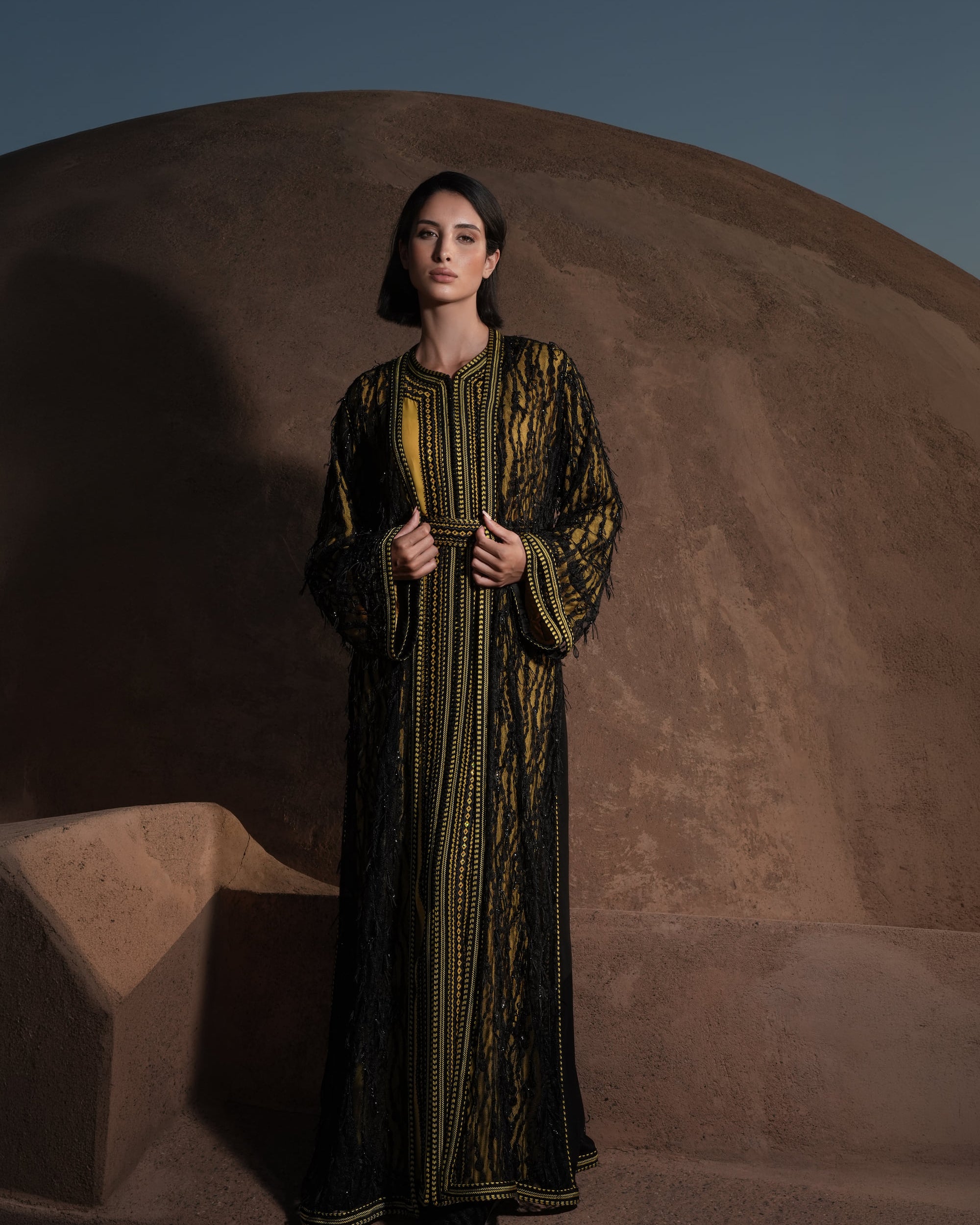 Onyx Serenade fringed black lace Moroccan kaftan over a mustard-gold dress, full-length view