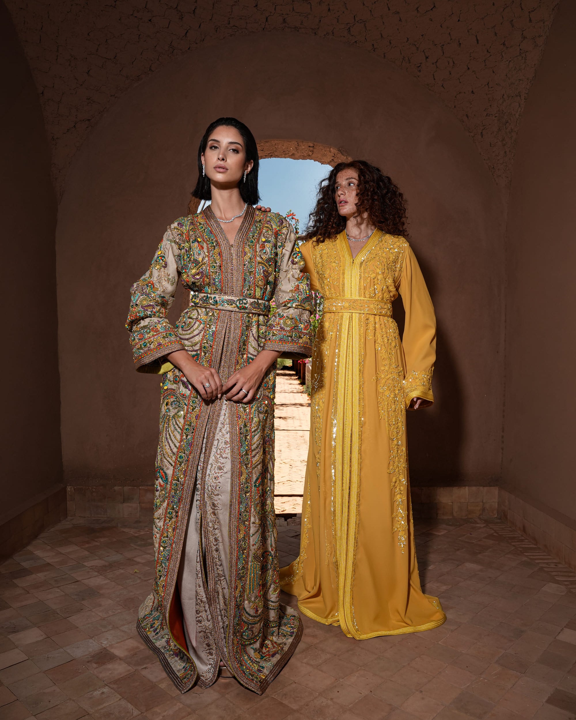 Saffron Vespers saffron crepe Moroccan kaftan with gold and silver embroidery, shown alongside a second look