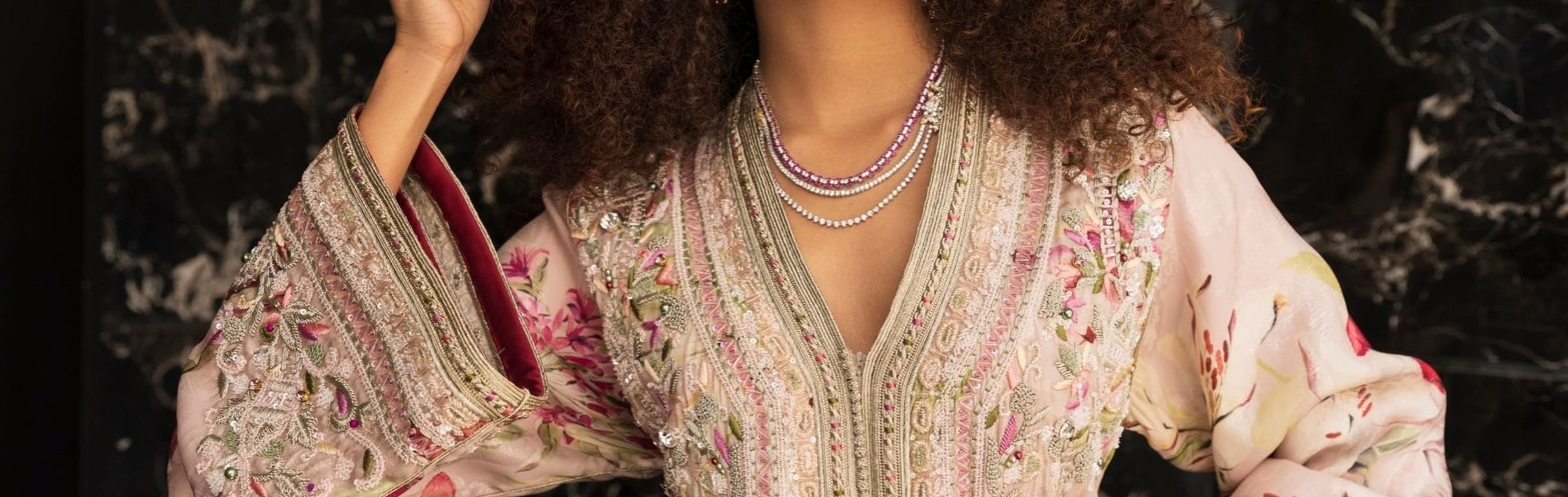 Blush floral Moroccan kaftan with a hand-embroidered placket, seen close against dark marble